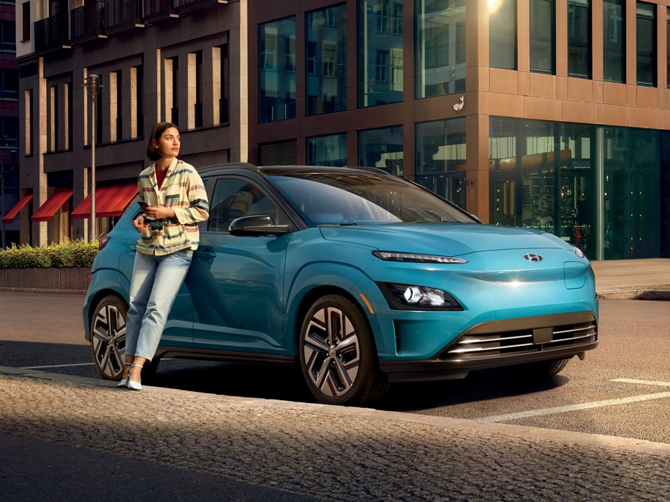 Image of a woman leaning on a parked surfy blue 2022 Kona Electric